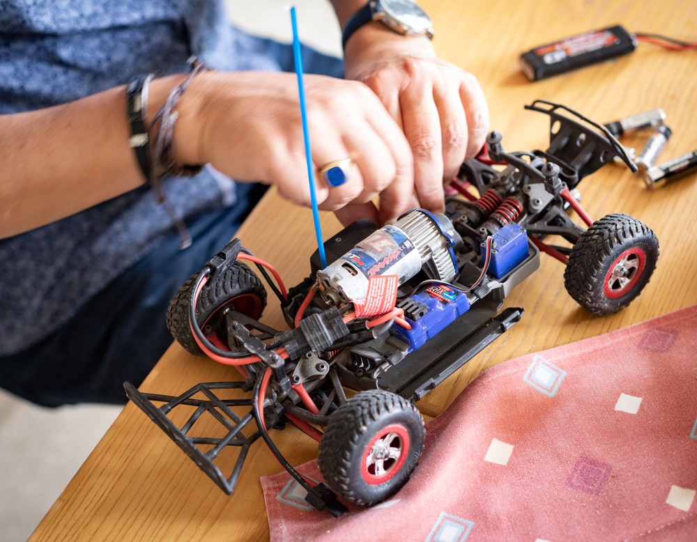 Zwei Hände reparieren ein Modellauto.