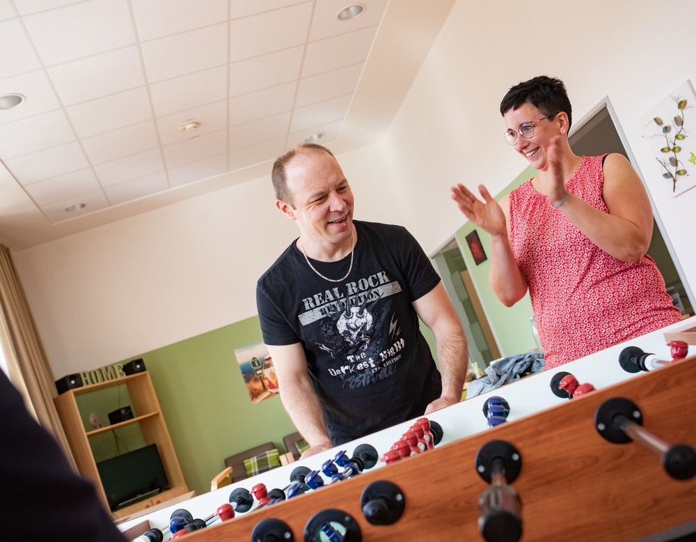 Ein Aufenthaltsraum in Warstein, in dem zwei leistungsberechtigte Personen und die Wohngruppenleitung am Kicker stehen.